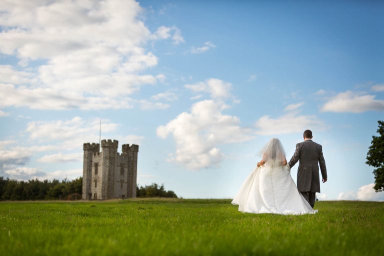 Bride and groom walking towards castle in scenic landscape by Southampton wedding photographer John Watson