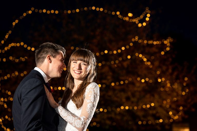 Smiling wedding couple under fairy lights at night by Southampton wedding photographer John Watson
