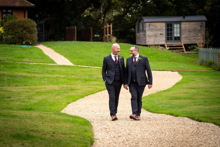 Two grooms walking on a path in a garden by Southampton wedding photographer John Watson