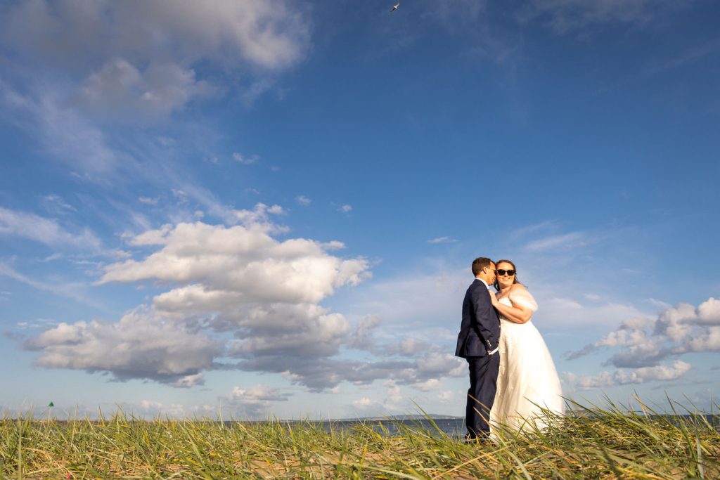 Bride and groom embrace on a sunny beach by Southampton wedding photographer John Watson