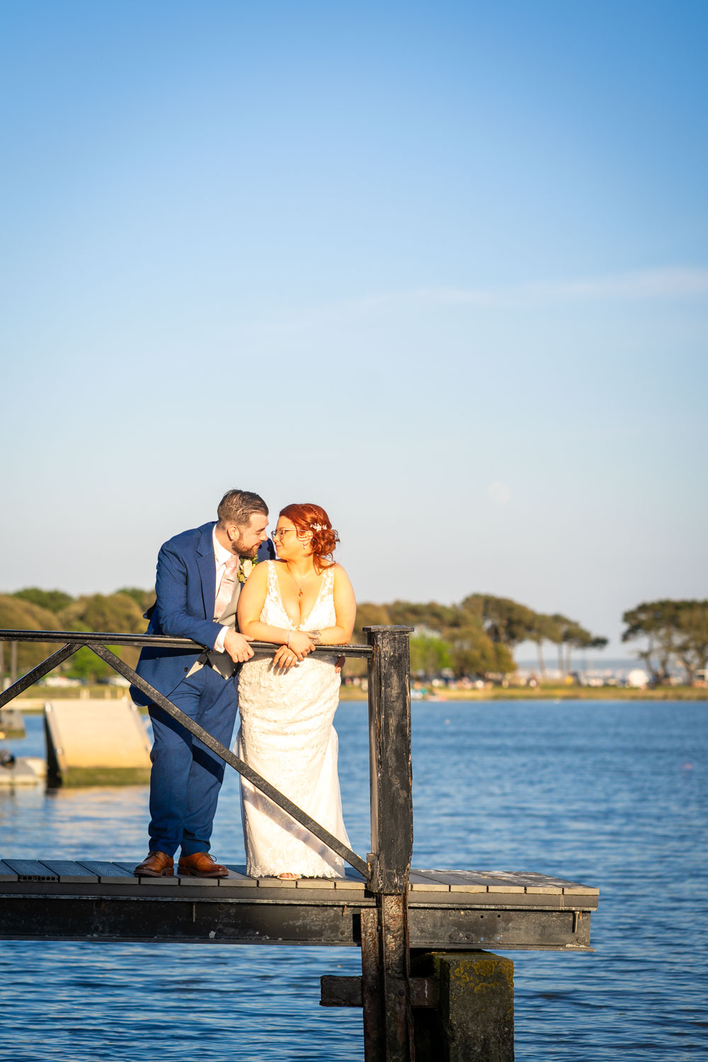 Bride and groom embrace by serene waterfront pier by Southampton wedding photographer John Watson