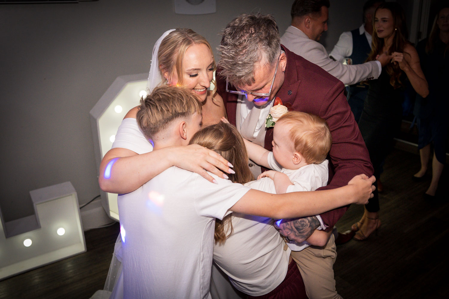 Bride and groom embrace children joyfully at wedding reception by Southampton wedding photographer John Watson
