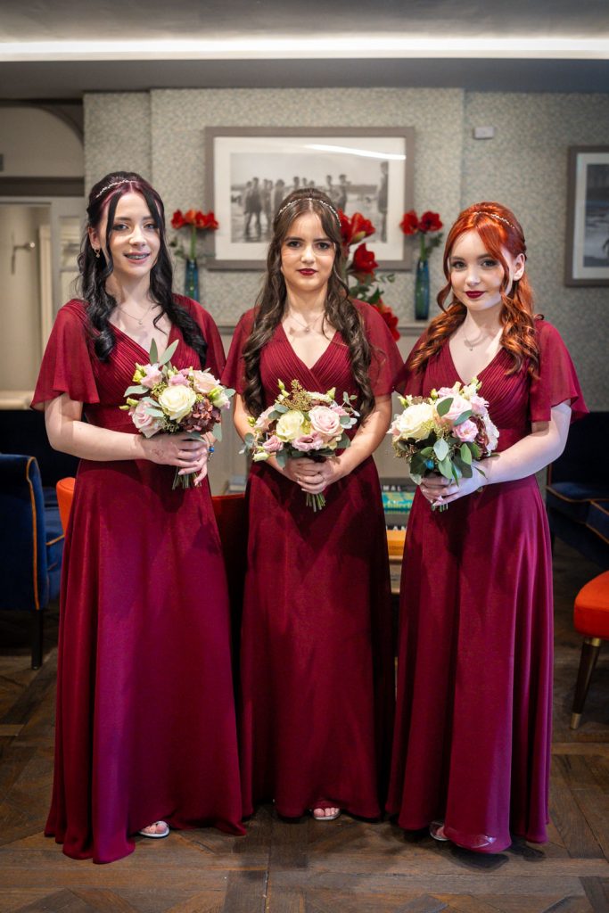 Three bridesmaids in red dresses holding bouquets by Southampton wedding photographer John Watson