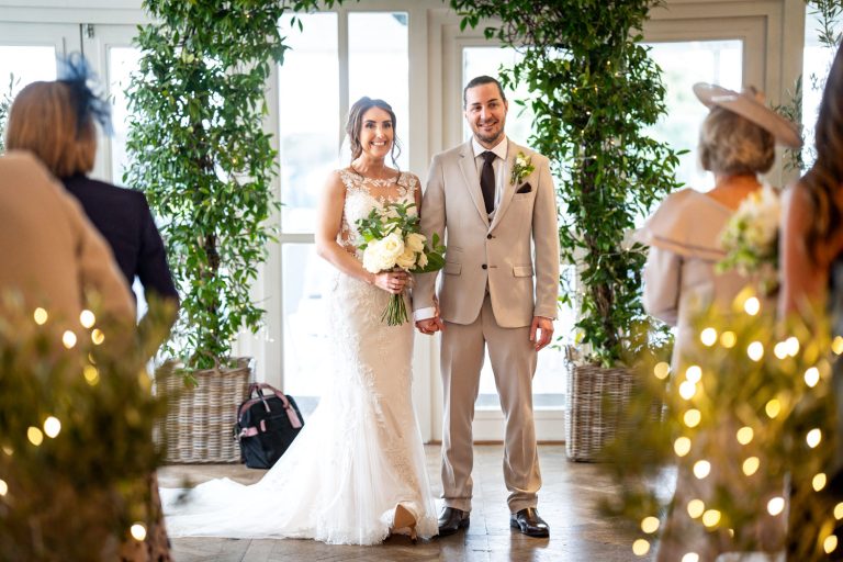 Bride and groom holding hands at elegant indoor ceremony by Southampton wedding photographer John Watson
