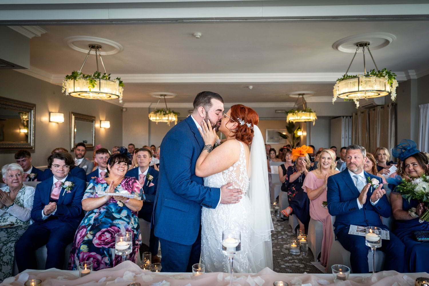 Bride and groom kiss at ceremony filled with guests by Southampton wedding photographer John Watson