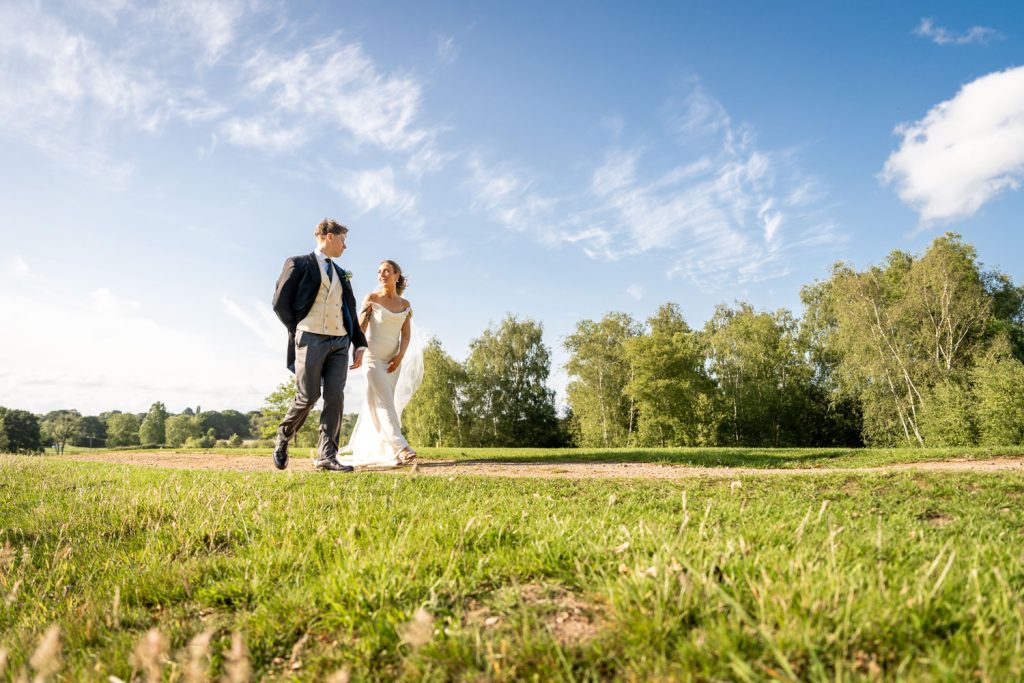 Bride and groom walking in sunlit park by Southampton wedding photographer John Watson
