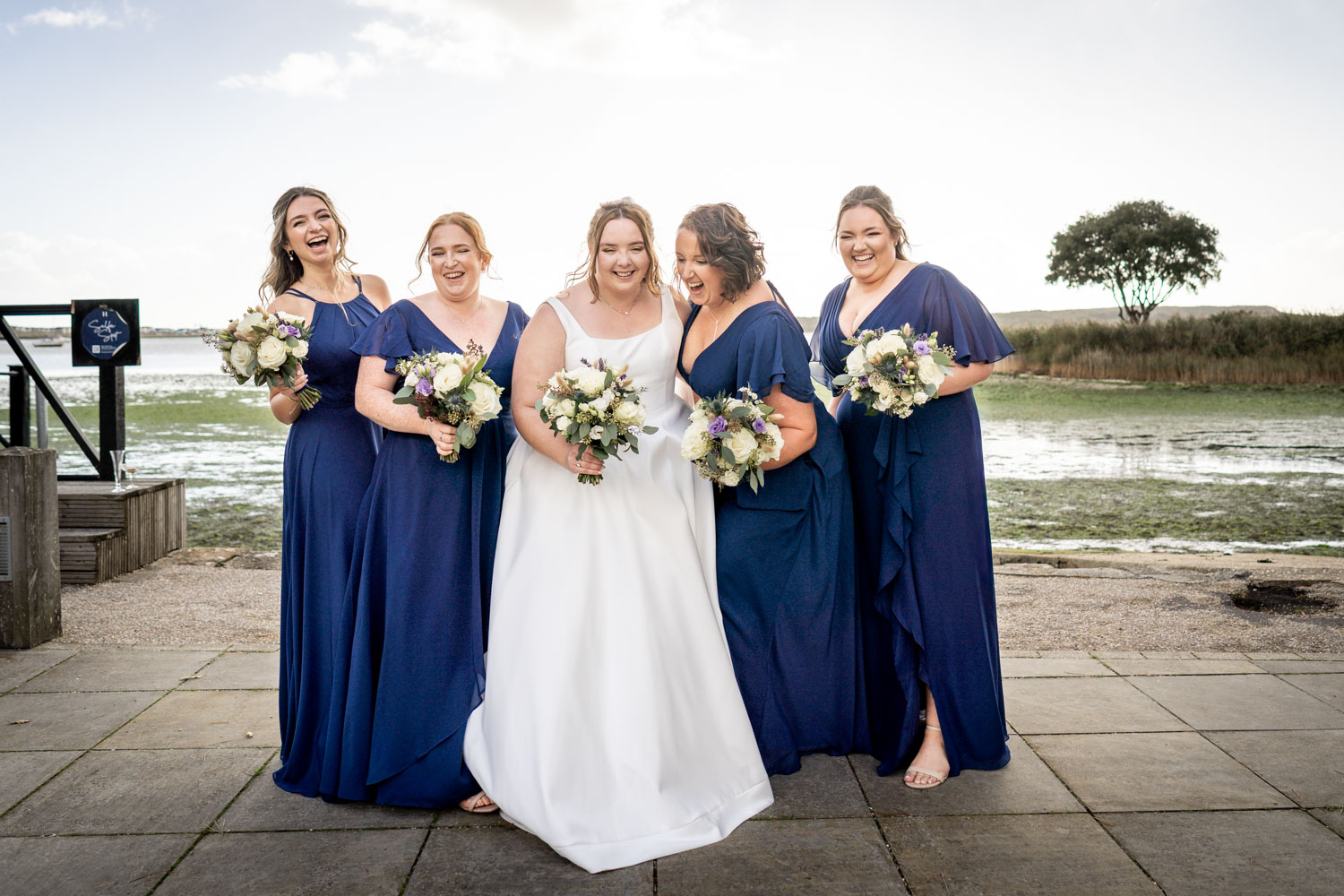 Bride and bridesmaids in blue dresses by the waterfront by Southampton wedding photographer John Watson