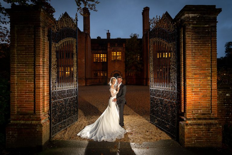 Bride and groom in front of manor gates at dusk by Southampton wedding photographer John Watson