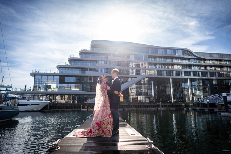 Bride and groom embrace by modern building by Southampton wedding photographer John Watson