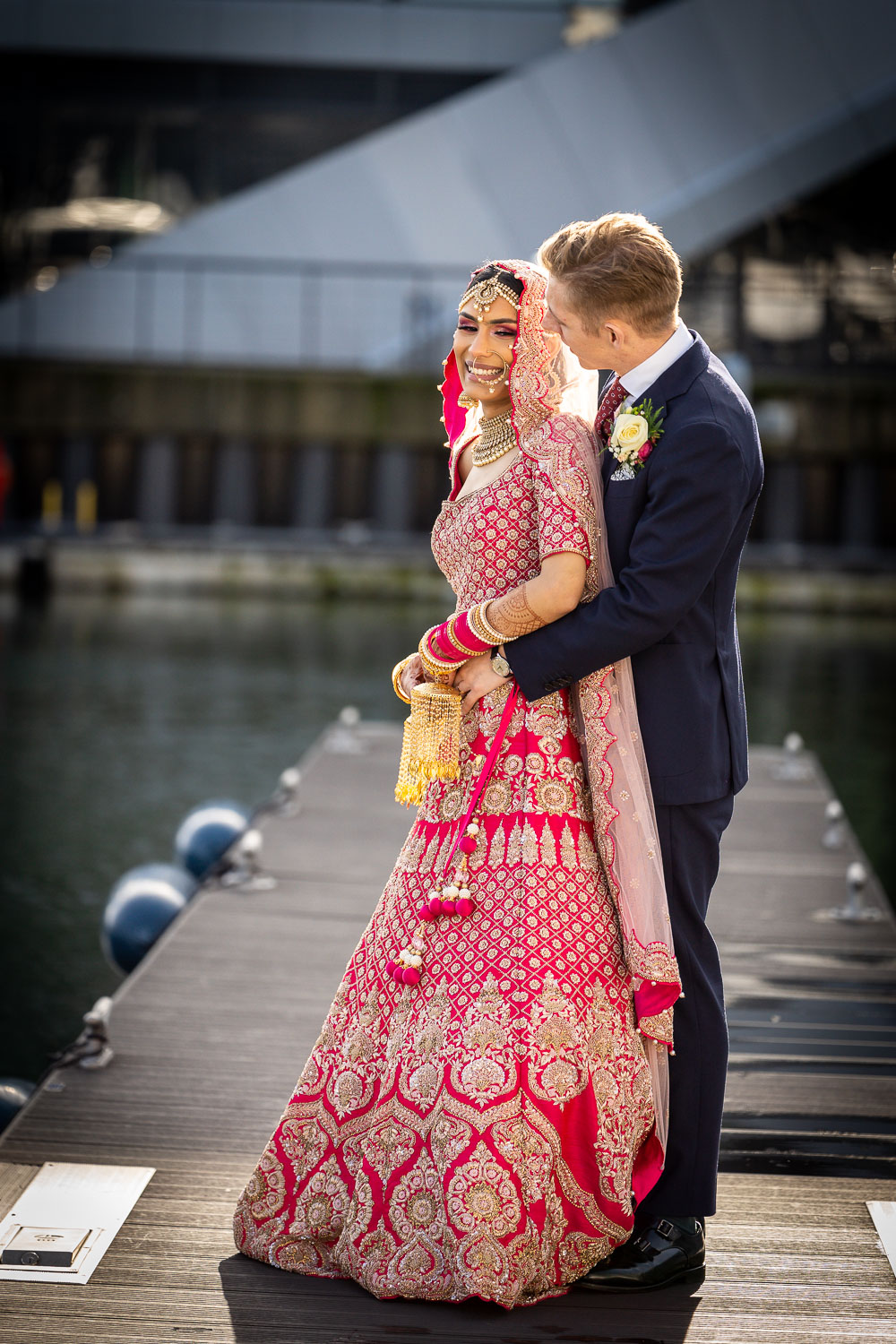 Bride and groom stand on pier in elegant wedding attire by Southampton wedding photographer John Watson