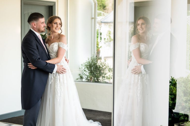 Bride and groom embrace reflecting in glass by Southampton wedding photographer John Watson