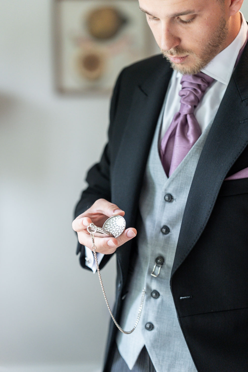 Groom holding a vintage pocket watch in elegant attire by Southampton wedding photographer John Watson