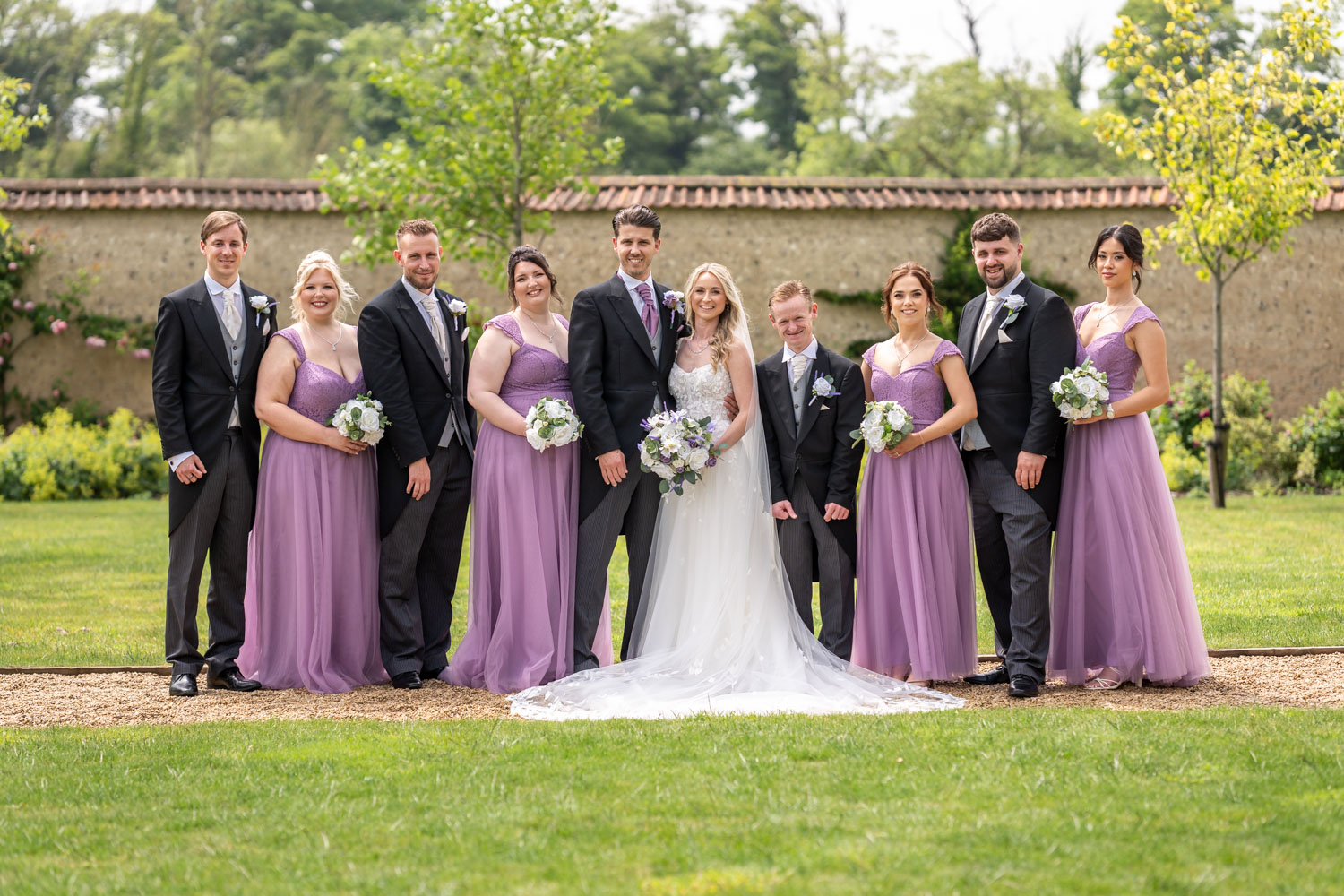 Bridal party posing in garden with purple dresses by Southampton wedding photographer John Watson