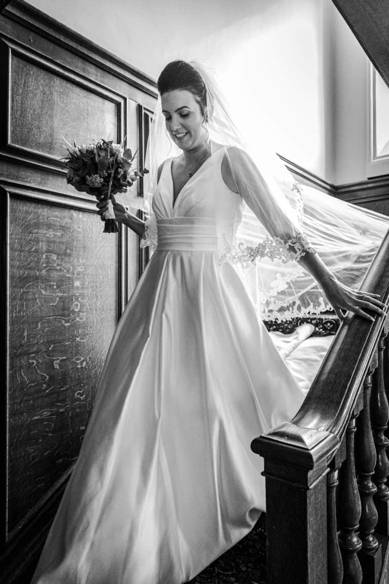 Bride descending staircase holding flowers by Southampton wedding photographer John Watson