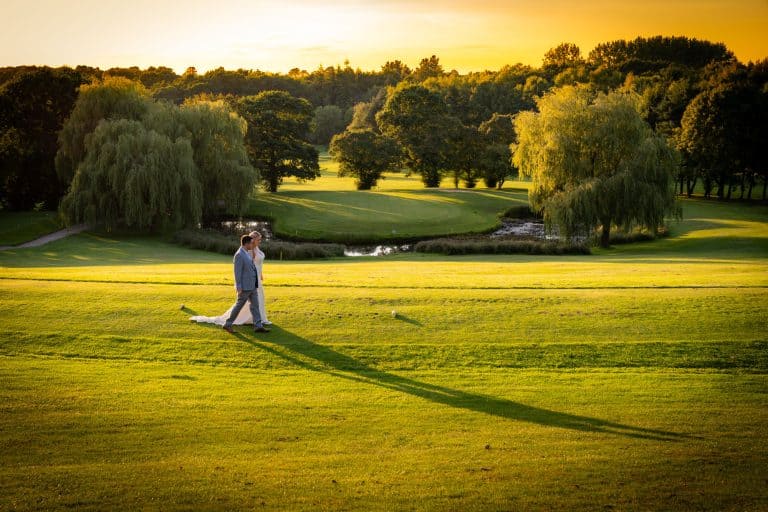 Bride and groom walking on golf course at sunset by Southampton wedding photographer John Watson