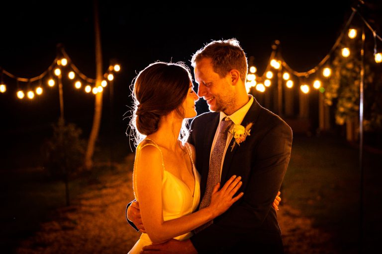 Bride and groom embrace under warm lights at night by Southampton wedding photographer John Watson