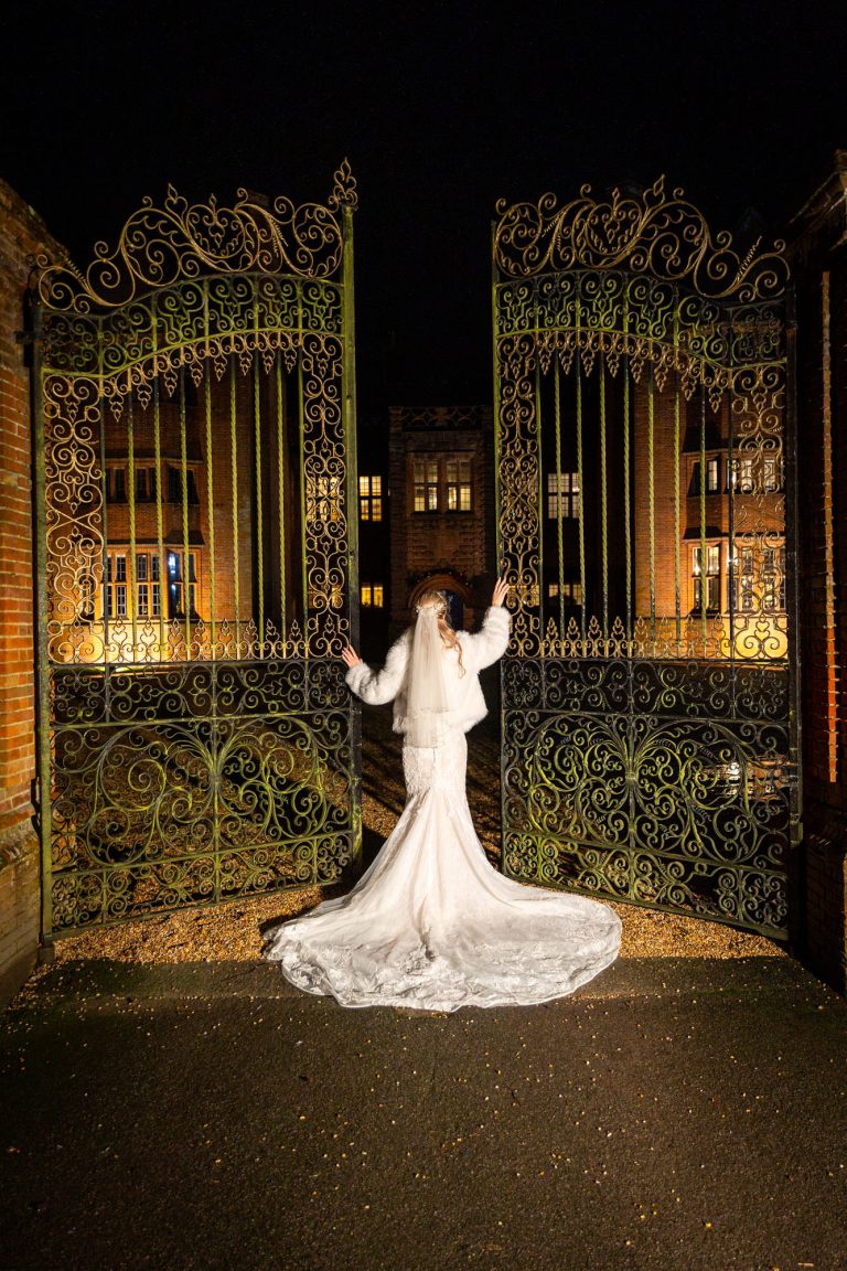 Bride in elegant gown at ornate gates by Southampton wedding photographer John Watson