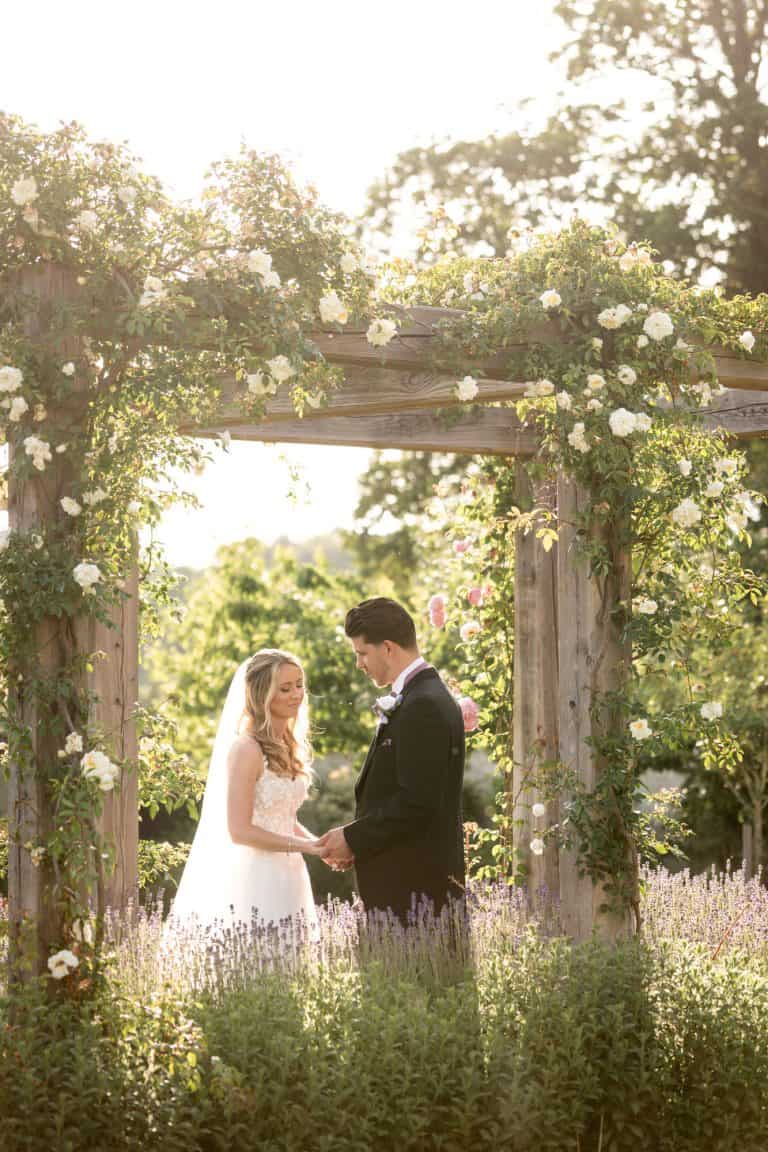 Bride and groom under floral arch in garden setting by Southampton wedding photographer John Watson