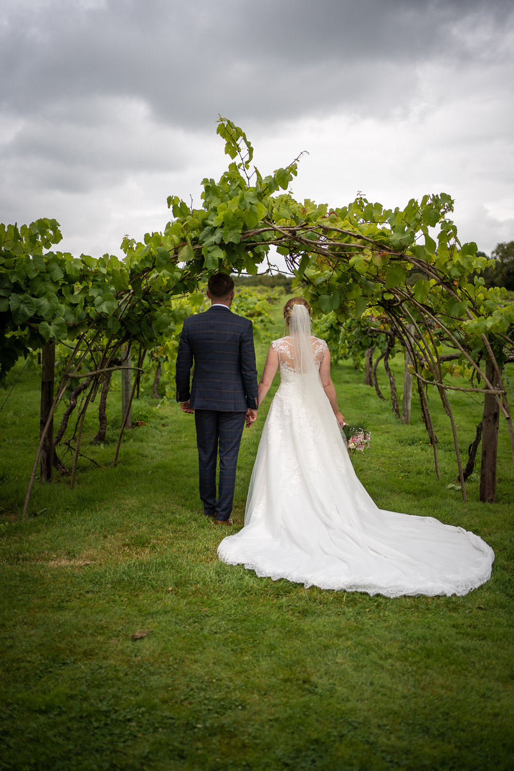 Bride and groom walking through vineyard arch by Southampton wedding photographer John Watson