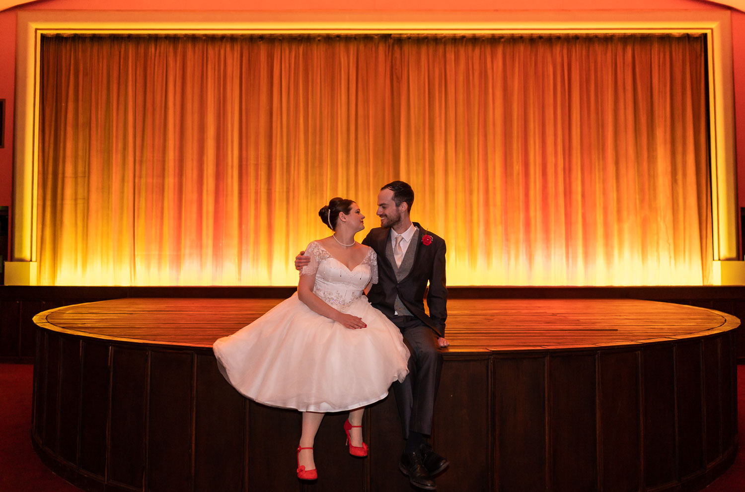 Bride and groom sitting on stage with warm lighting by Southampton wedding photographer John Watson