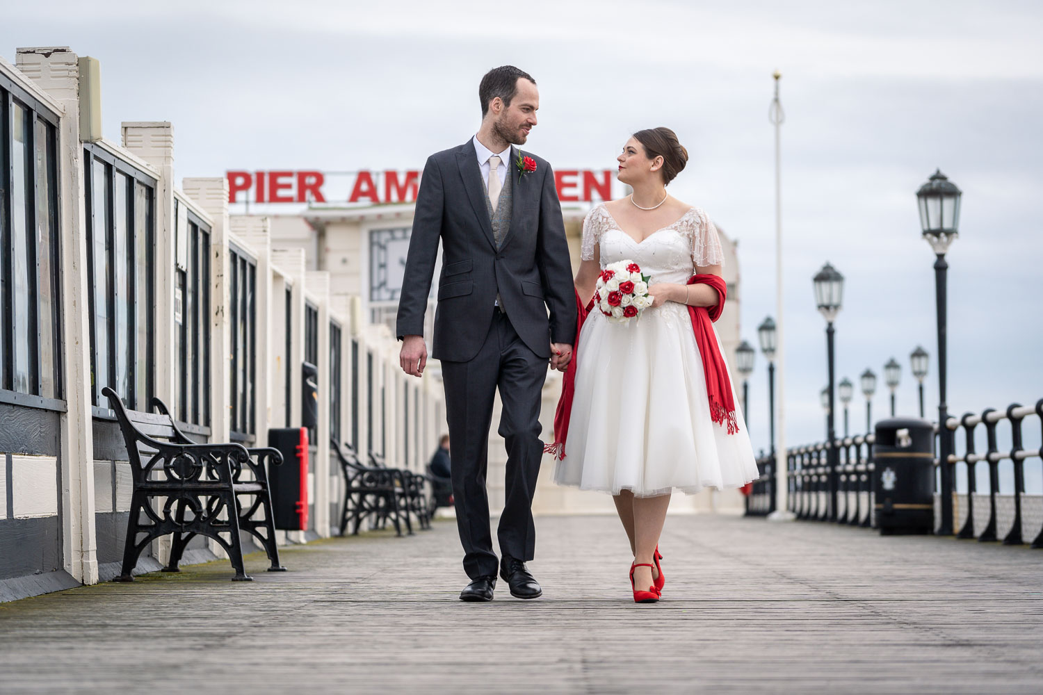 Bride and groom walking on pier in elegant wedding attire by Southampton wedding photographer John Watson