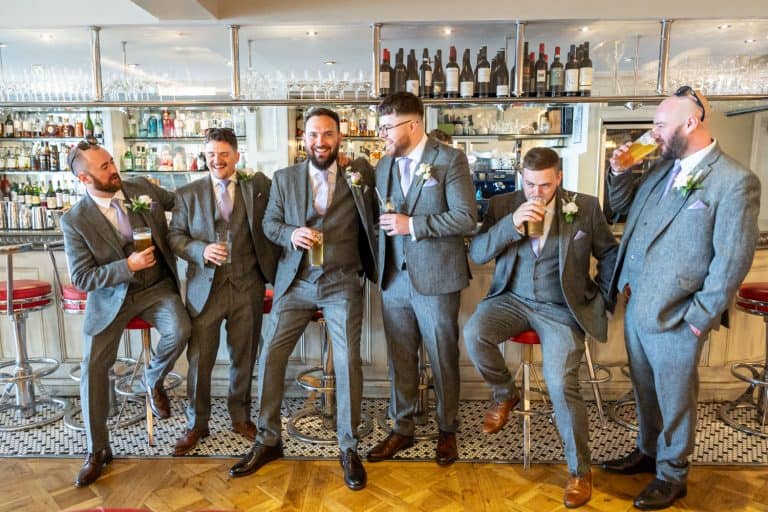 Groomsmen in suits enjoying drinks at bar by Southampton wedding photographer John Watson