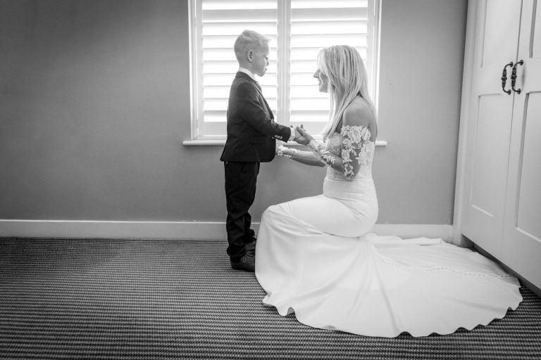 Bride kneeling with young boy in wedding attire by Southampton wedding photographer John Watson