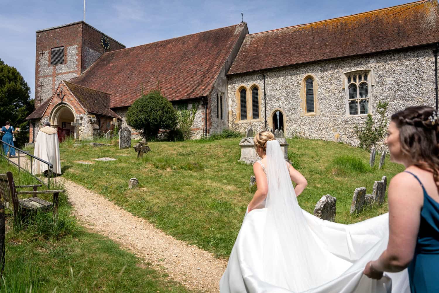 Bride walks to picturesque church on sunny wedding day by Southampton wedding photographer John Watson