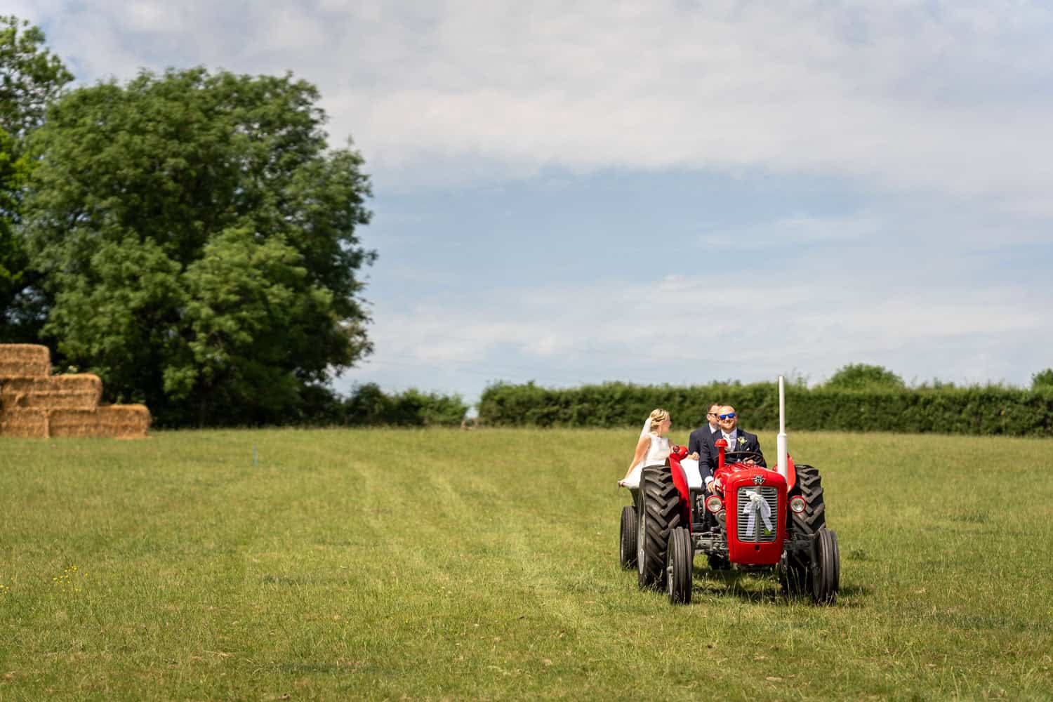 Bride and groom on tractor in sunny field by Southampton wedding photographer John Watson