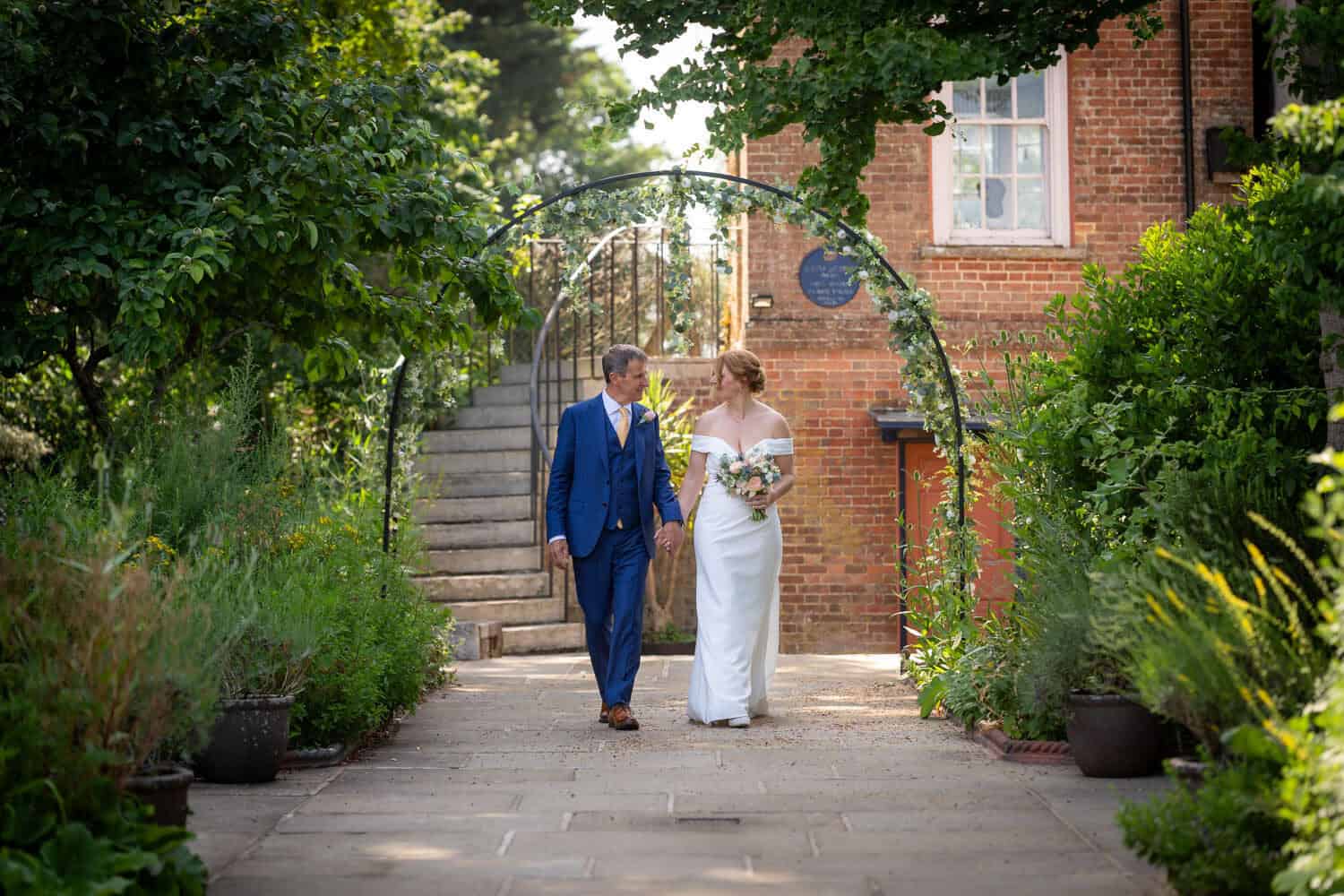 Bride and groom walking in garden pathway by Southampton wedding photographer John Watson