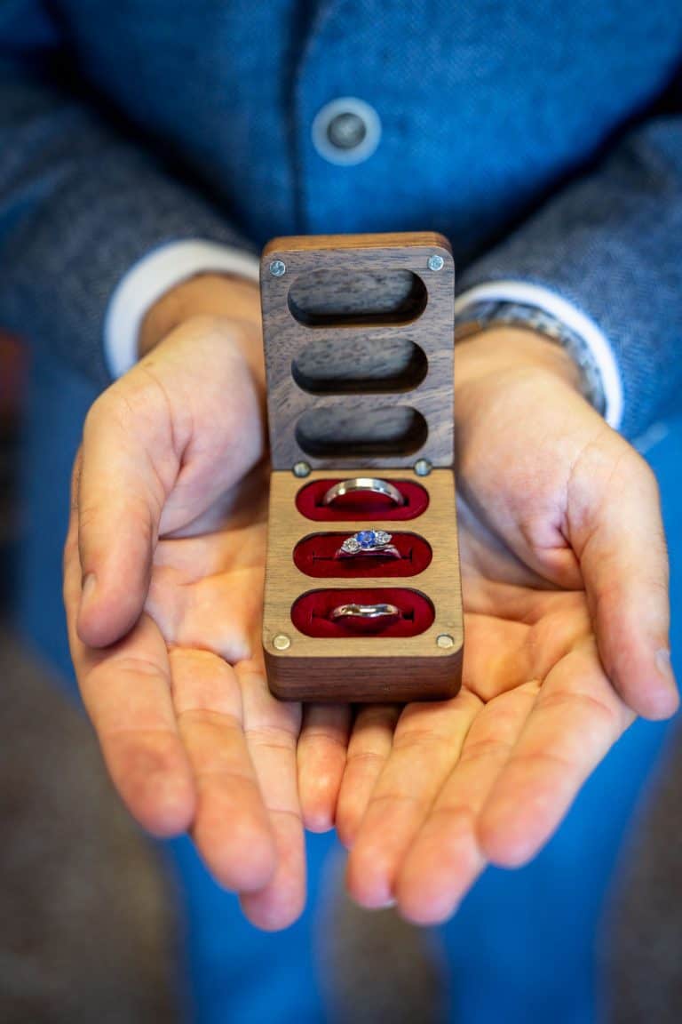 Wooden ring box held by groom in blue suit by Southampton wedding photographer John Watson