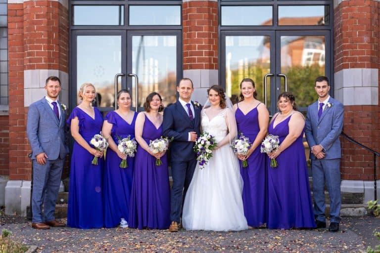 Wedding party in purple dresses and suits outside venue by Southampton wedding photographer John Watson